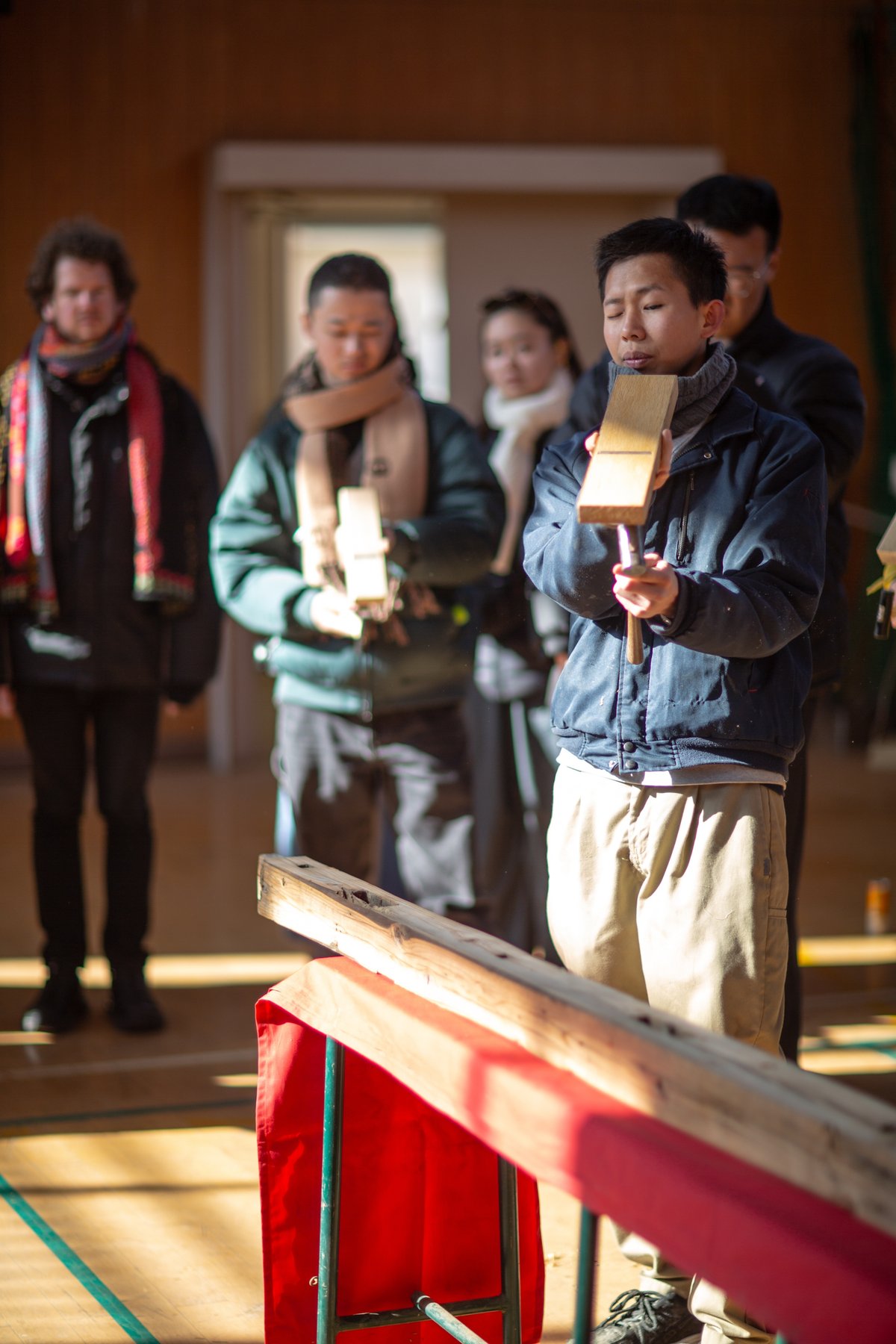 Visiting students learning to plane reclaimed wood under master carpenter Mr. Shikata inside the Sunoue gymnasium
